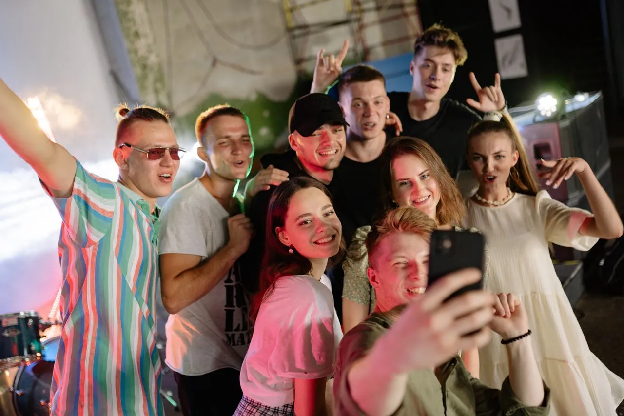 Freundesgruppe macht abends vor einer Bühne ein ausgelassenes Gruppenselfie