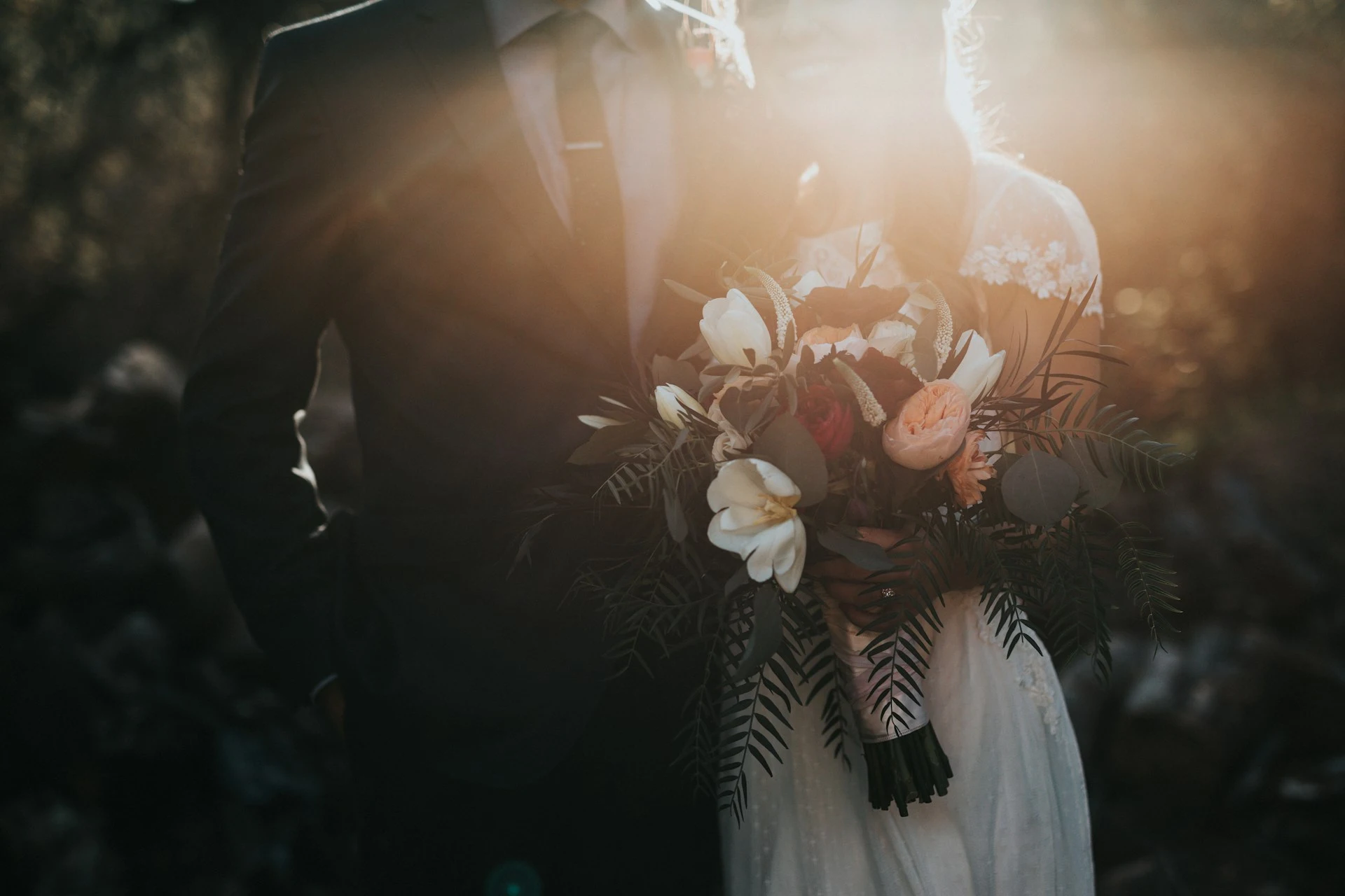 Nahaufnahme eines Hochzeitspaares im Sonnenlicht mit großem Blumenstrauß